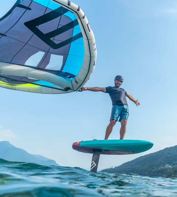 A rider on a wing foil board, flying above the water with the wing overhead.