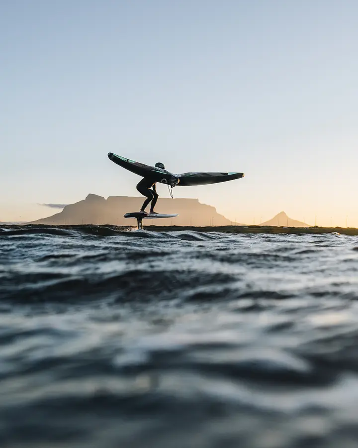 A rider wing foiling on calm water at sunset.