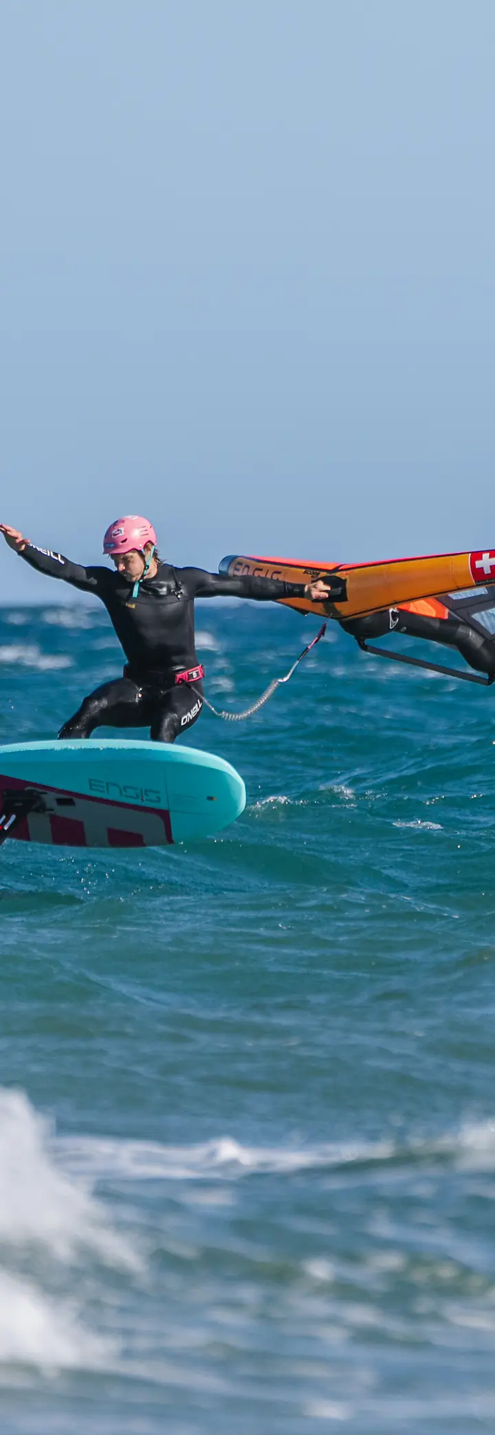 A wing foil rider in a wetsuit riding fast through choppy water, the wing held out to the side.